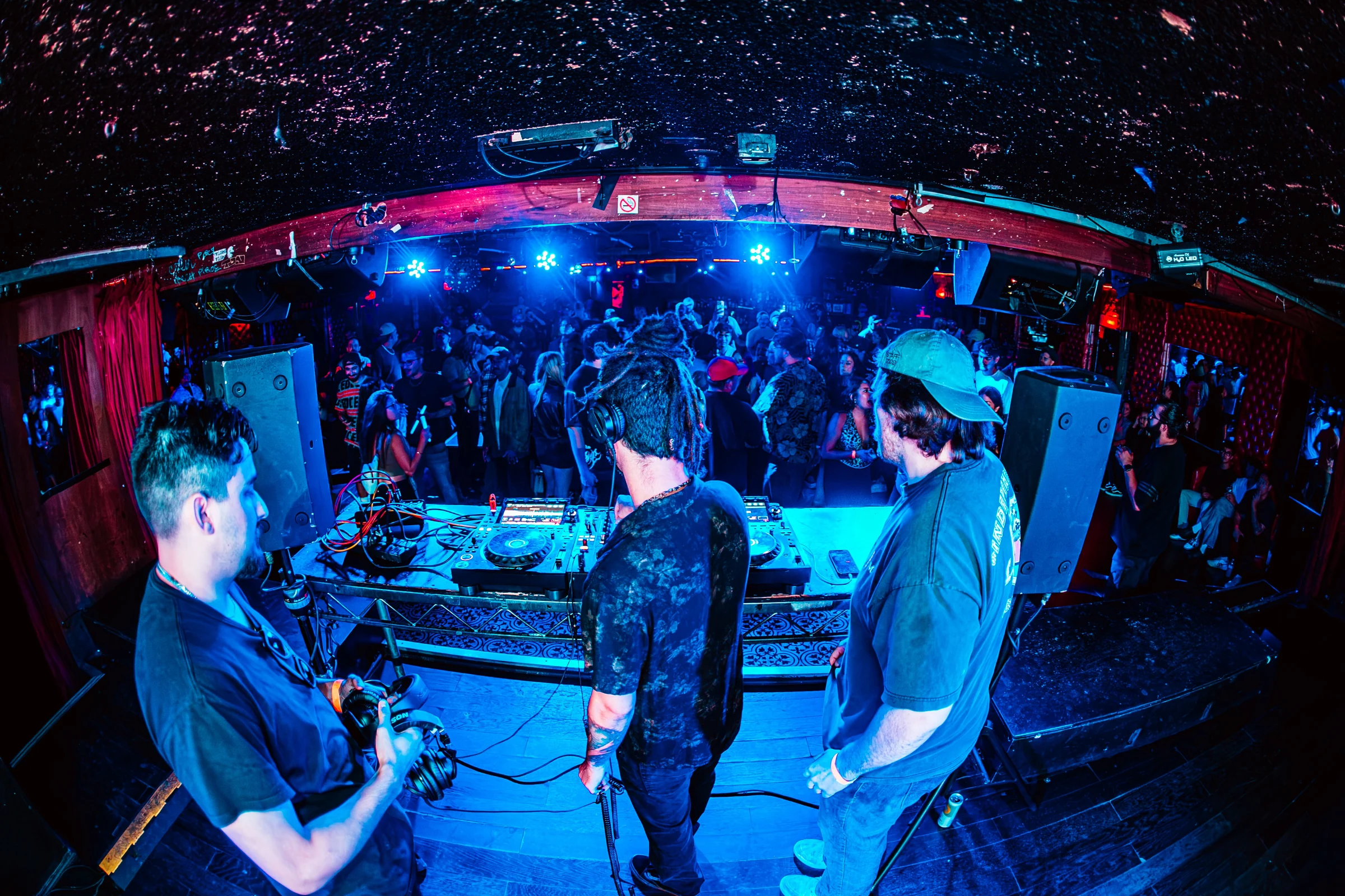 View from the DJ booth toward a crowded club under blue and red lights